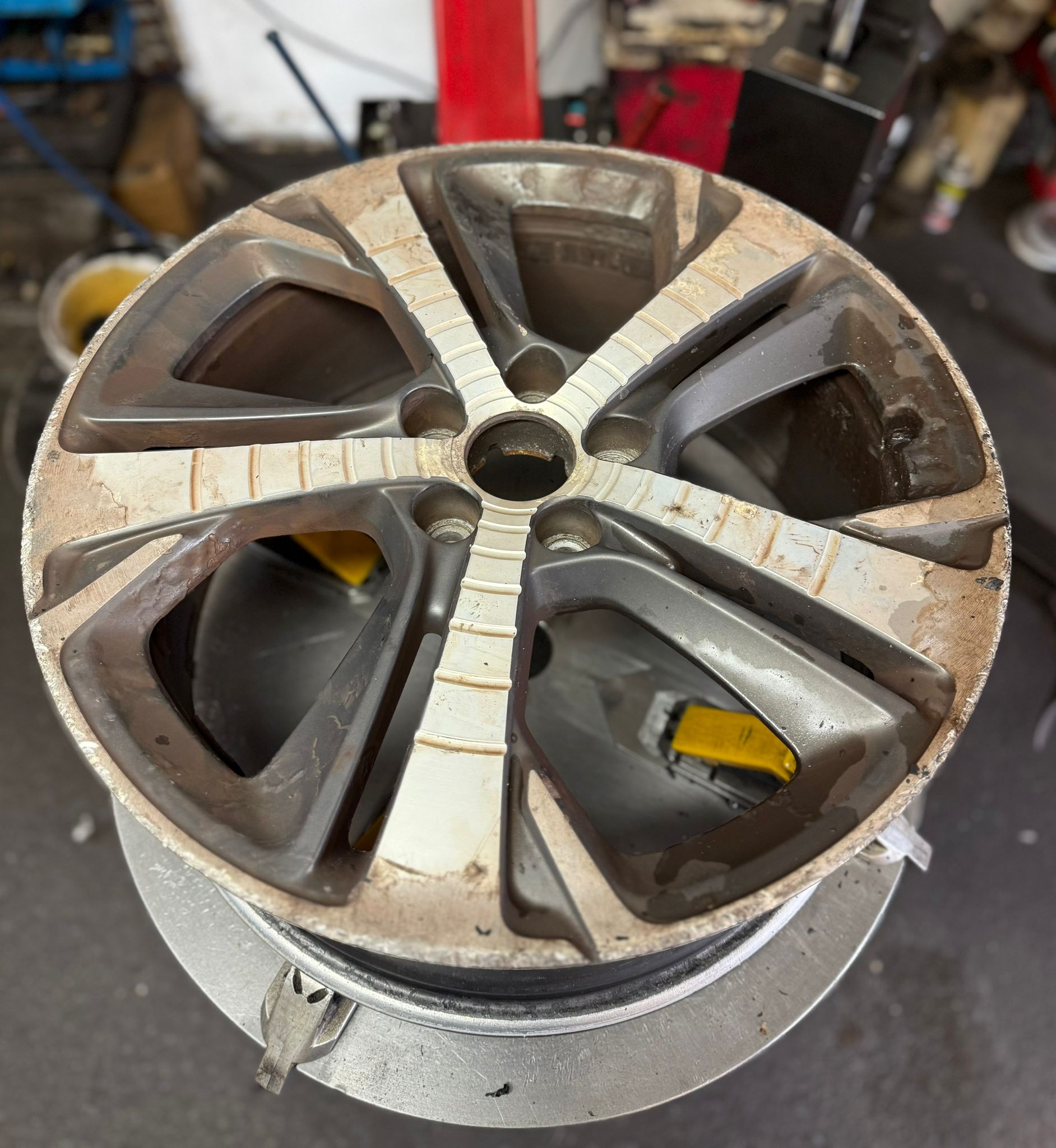 Before — Faded, lacquer-peeled silver wheel refinished in a tough gunmetal grey powder coat. — Burnley